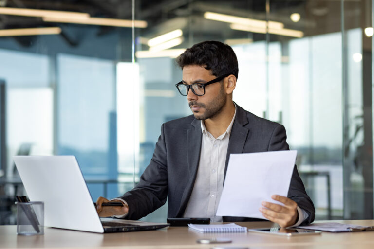 Serious concentrated hispanic businessman financier on paperwork inside office, man in business suit at workplace reviewing and reading papers, contracts and accounts reports